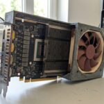デスクトップPCの作業台に設置された、3Dプリンター製カスタムファンケースに収められたAMDサーバーアクセラレーターカード。HBM2メモリスタックの基板が露出した状態でリアルに描写