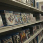 薄暗いゲームショップの陳列棚、まばらに残ったPS用パッケージソフト、埃っぽく寂れた雰囲気、ノスタルジックな構図